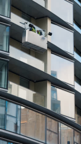 Vertical-Video-Of-Workmen-In-Inspection-Cradle-Outside-Luxury-Housing-Apartments-At-Battersea-Power-Station-Development-In-London-UK-